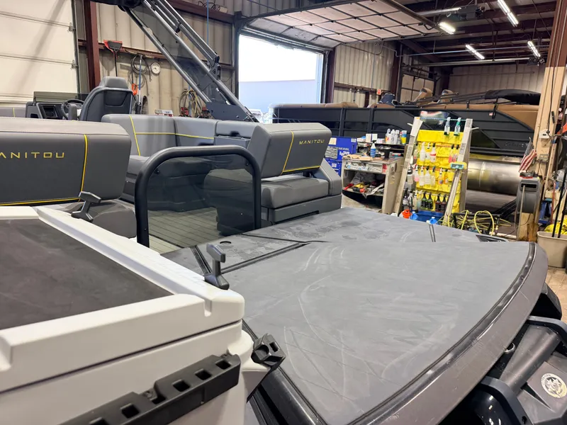 Slide: The Image of The image shows the rear of a Manitou 22 Explore Tritoon with gray upholstery in a workshop. - 49