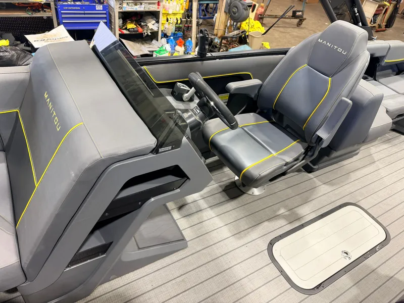 Slide: The Image of The image shows the helm of a Manitou 22 Explore Tritoon with gray seats and yellow stitching. - 19