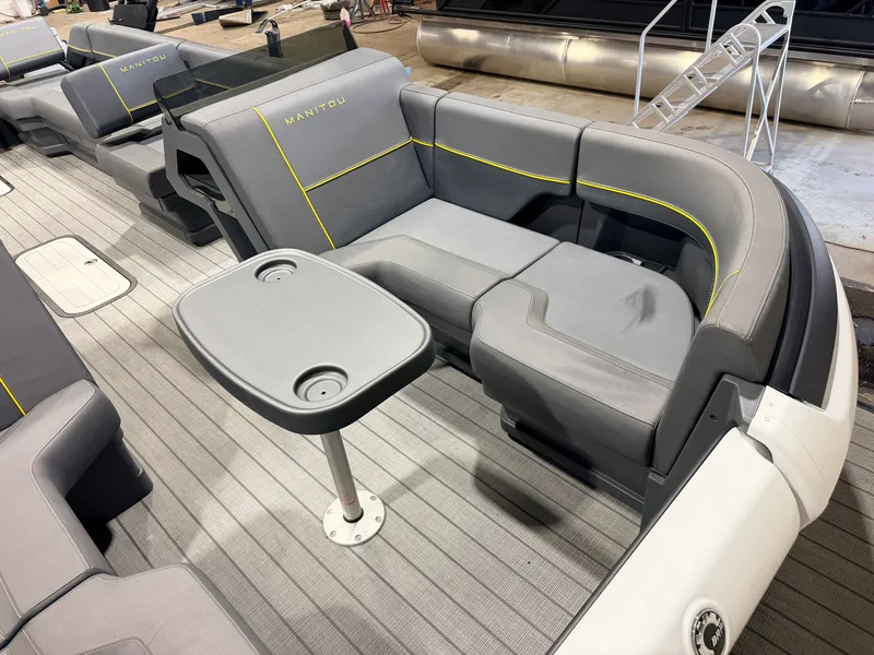 Slide: The Image of The image shows the gray and yellow seating area of a Manitou 22 Explore Tritoon with a small table. - 10