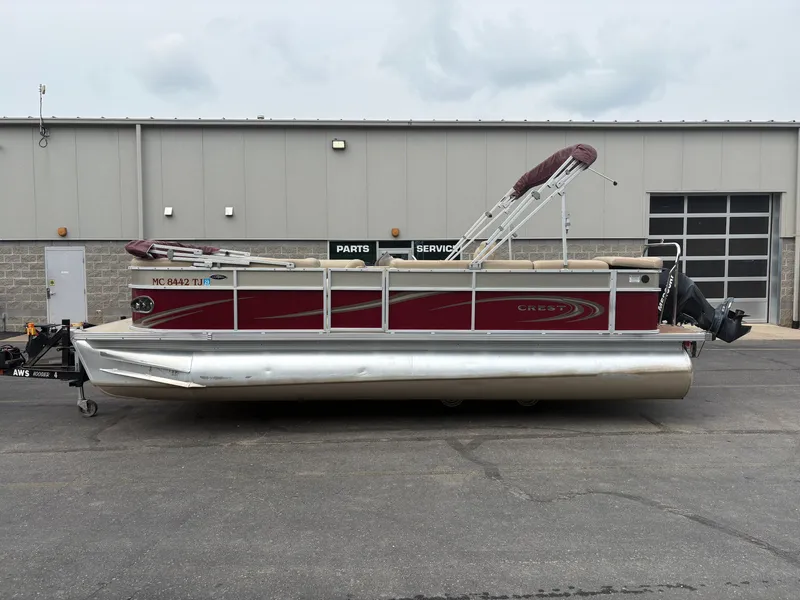 The Image of A red pontoon boat, Crest Classic 230L model from 2012, is parked in front of a building. - 1