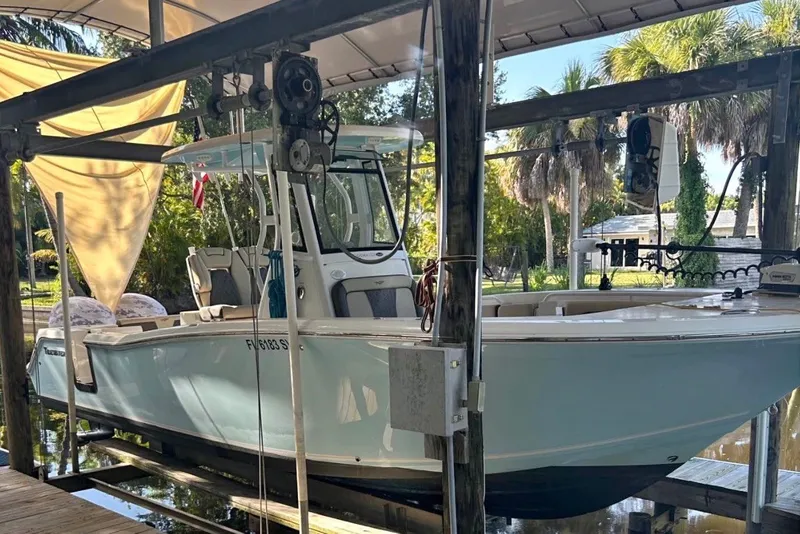 Slide: The Image of 2021 Tidewater 272 CC Adventure boat docked under a canopy with lush greenery. - 0