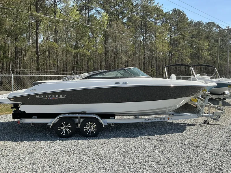 The Image of A 2025 Monterey M-22 boat on a trailer in a gravel lot, surrounded by trees. - 1