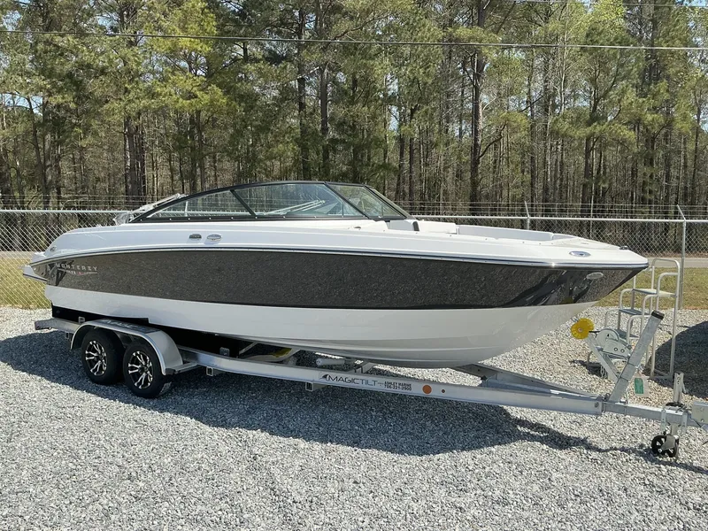 Slide: The Image of A 2025 Monterey M-22 boat on a trailer in a gravel lot, surrounded by trees. - 3