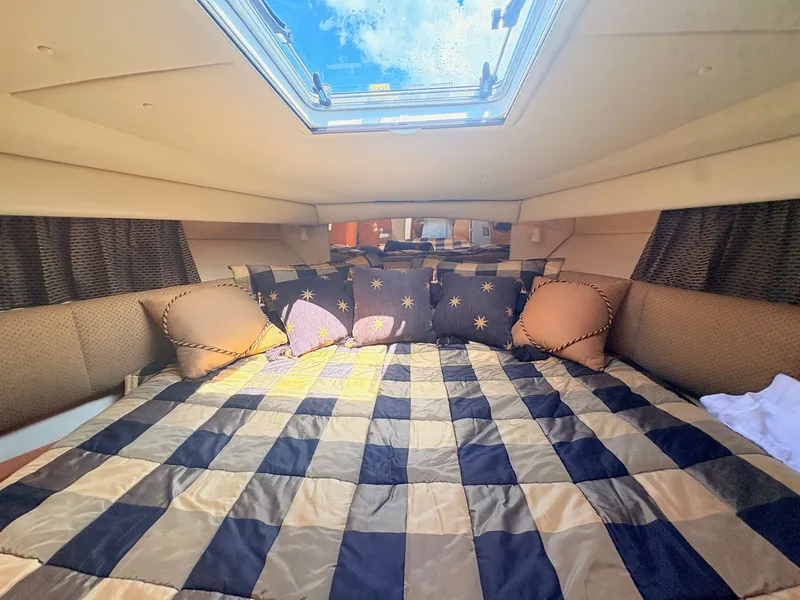 Slide: The Image of The cabin of the 2007 Chaparral Signature 350 features a cozy bed with a checkered bedspread and several pillows. A skylight lets in natural light. - 14