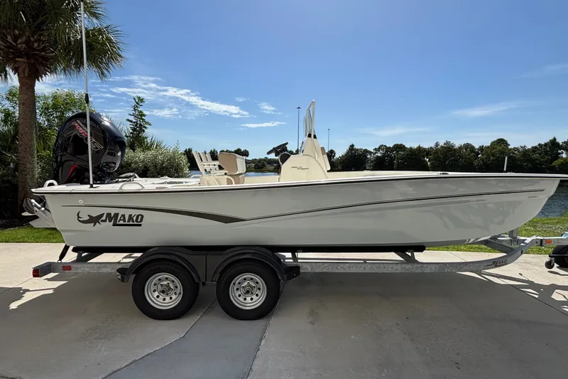 The Image of 2026 Mako Pro Skiff 19 CC boat on trailer, parked near water under clear blue sky. - 0