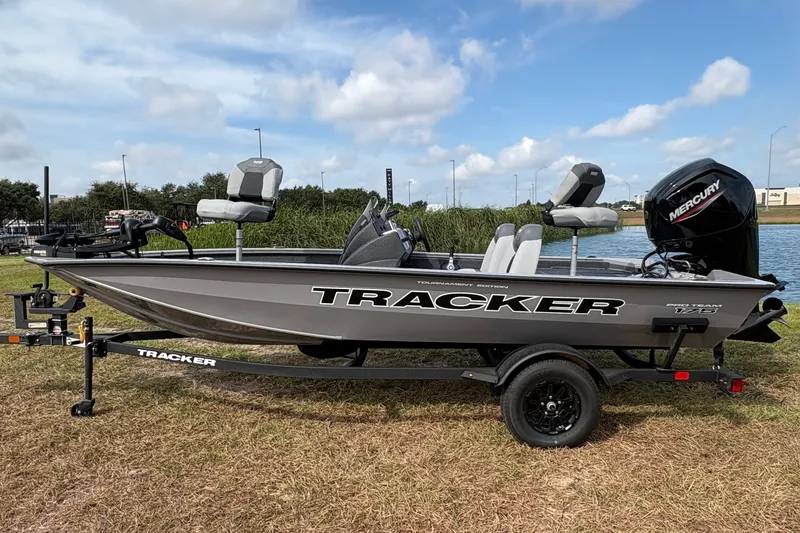 The Image of 2027 Tracker Pro Team 175 boat on trailer by a lake under blue sky. - 2