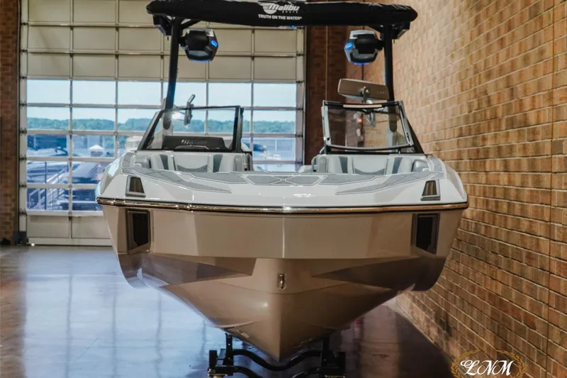 Slide: The Image of 2027 Malibu M230 boat in showroom, sleek design, brick wall background. - 4