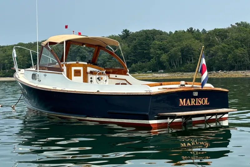 The Image of Classic 1978 Wasque 26 boat named "Marisol" on calm water, with forested shoreline background. - 0