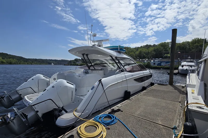 The Image of 2025 Four Winns TH36 yacht docked by a scenic waterfront under a partly cloudy sky. - 0