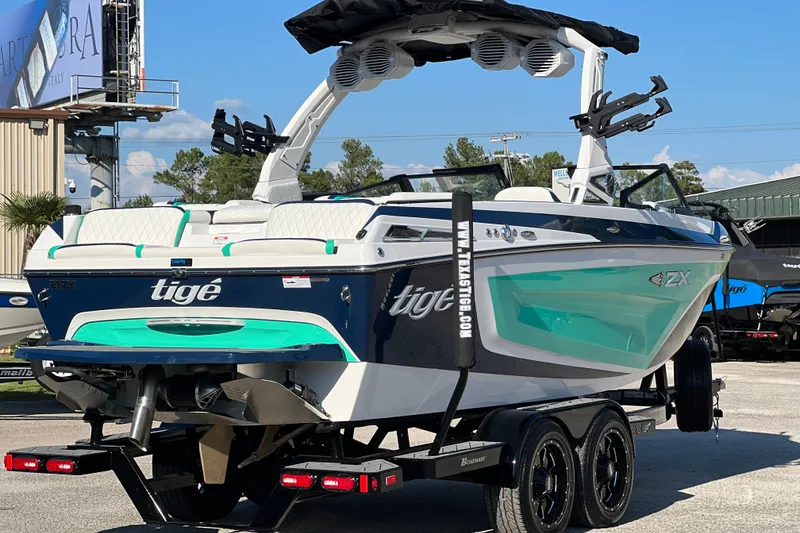 Slide: The Image of 2023 Tigé 21ZX boat on trailer, featuring sleek design and vibrant teal accents. - 2