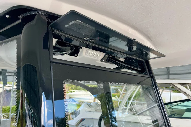 Slide: The Image of 2027 Robalo R230 Center Console boat windshield and roof detail in a marina setting. - 30