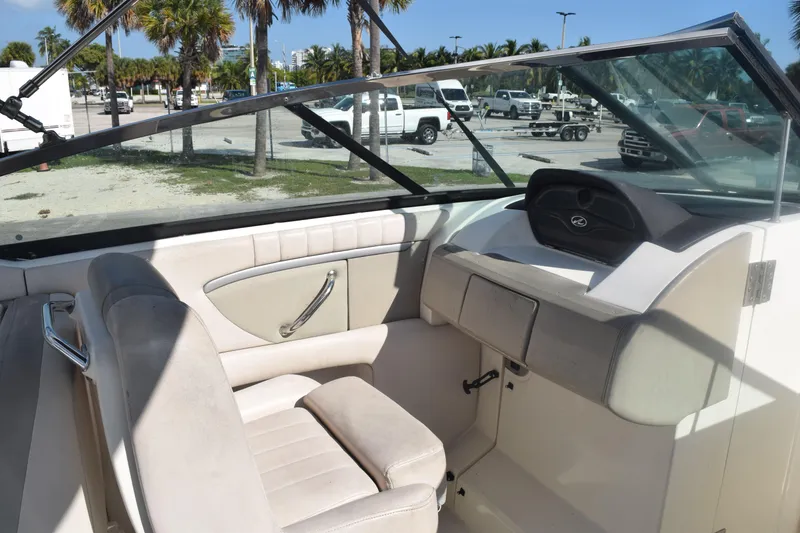 Slide: The Image of 2005 Sea Ray SLX 280 boat interior with beige seating and dashboard, parked outdoors. - 28