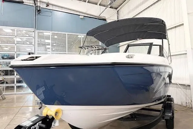 The Image of 2026 Yamaha Boats SX220 in showroom, featuring sleek blue and white design with canopy. - 7