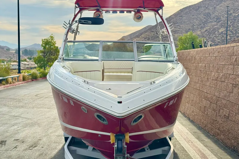 Slide: The Image of 2012 Cobalt 262 WSS boat with red hull, parked on a trailer, scenic mountain backdrop. - 2