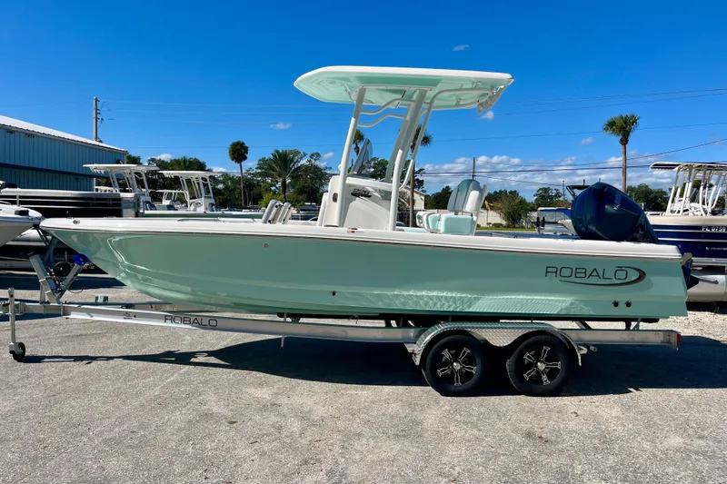 The Image of 2027 Robalo 226 Cayman boat on trailer, parked outdoors under clear blue sky. - 0