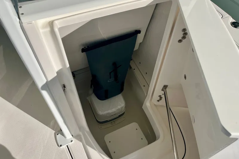 Slide: The Image of Storage compartment in 2027 Robalo 226 Cayman boat, featuring a blue bag and white container. - 24