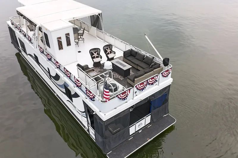 Slide: The Image of 2005 Sumerset houseboat with decorated deck, outdoor seating, and American flag on calm water. - 7
