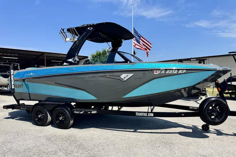 The Image of 2022 Tigé Z3 boat on trailer, blue and gray design, parked outdoors with American flag. - 1