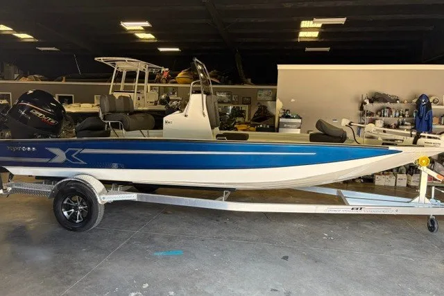Slide: The Image of 2027 Xpress H20 Bay boat in showroom, blue and white design, on trailer. - 2