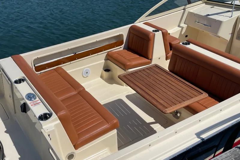 Slide: The Image of 2022 Rossiter 20 boat interior with brown leather seats and wooden table on water. - 23
