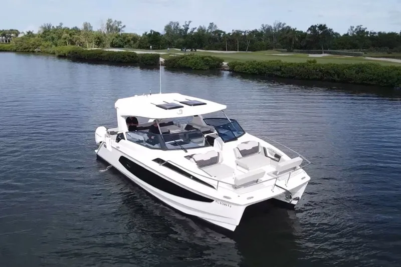 Slide: The Image of 2023 Aquila 36 Sport boat cruising on a calm river with lush greenery. - 1