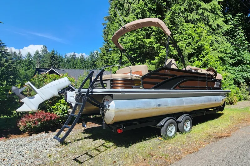Slide: The Image of 2023 Bennington 22 LSB pontoon boat on trailer, surrounded by lush greenery. - 21