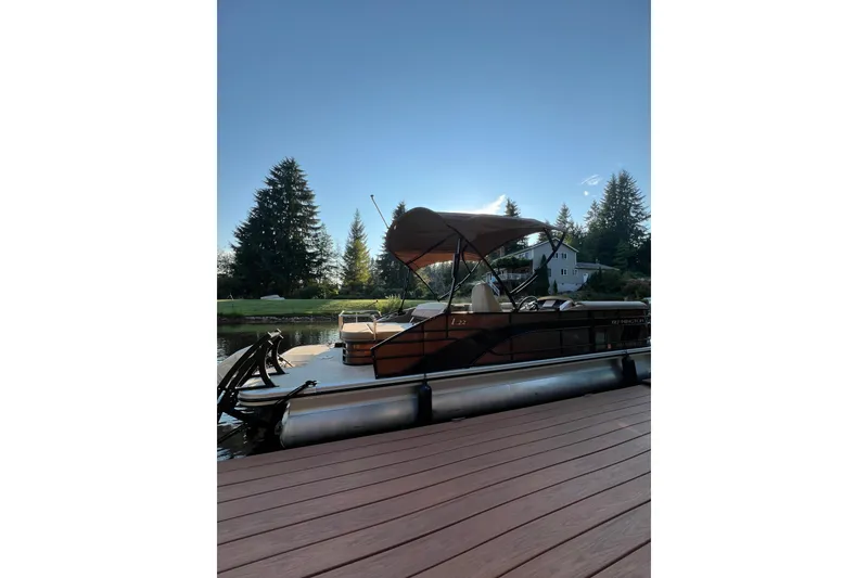 Slide: The Image of 2023 Bennington 22 LSB pontoon boat docked on a serene lake with trees in the background. - 20