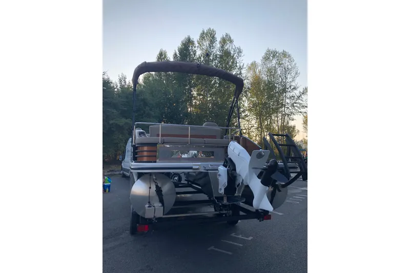 Slide: The Image of 2023 Bennington 22 LSB pontoon boat on trailer, parked outdoors with trees in background. - 11