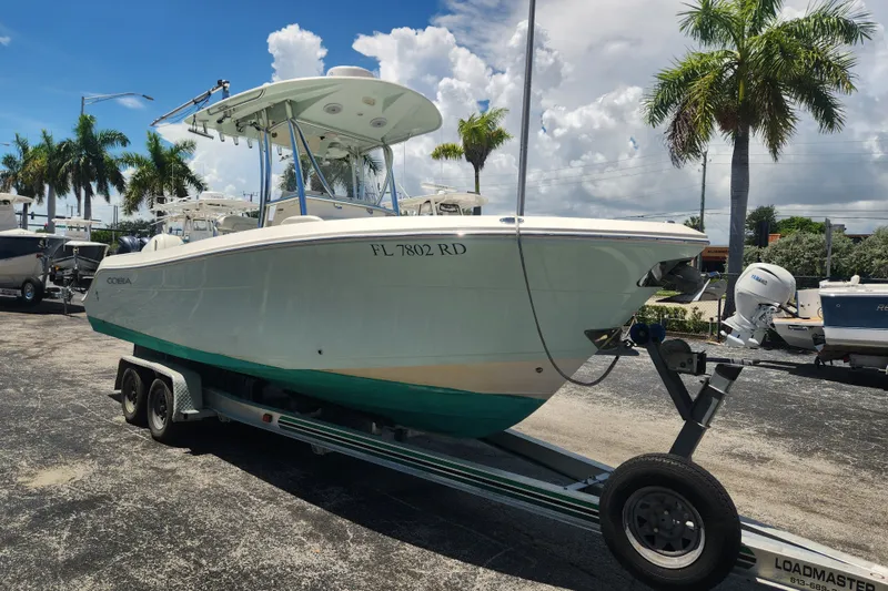 Slide: The Image of 2016 Cobia 237 Center Console boat on trailer, parked with palm trees in background. - 1