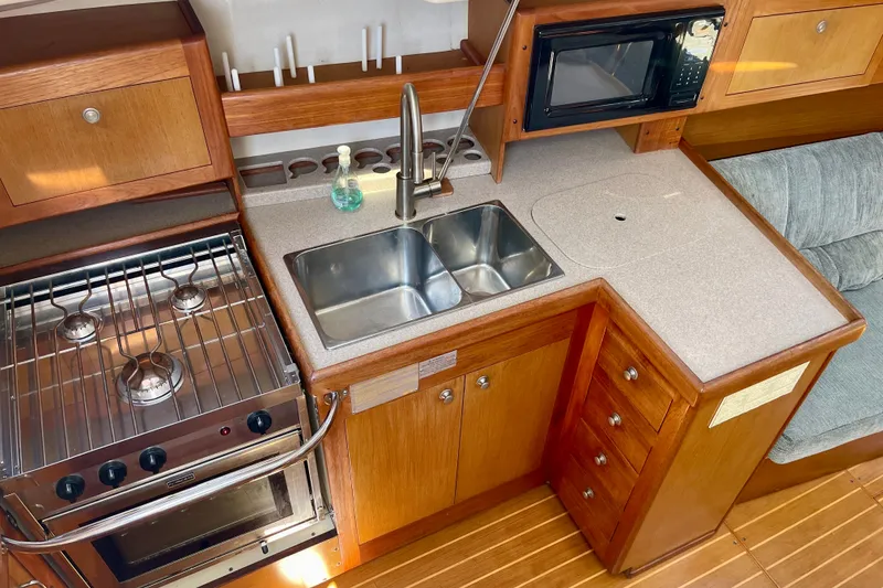 Slide: The Image of 1999 Hunter Passage 420 yacht kitchen with stove, sink, and microwave in wooden cabinetry. - 26