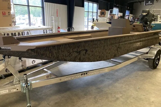 The Image of 2026 Xpress Bayou 180CC boat on trailer in showroom, featuring camouflage design. - 1