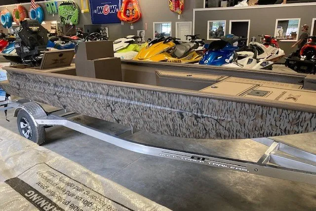 Slide: The Image of 2026 Xpress Bayou 180CC boat on trailer in showroom with jet skis. - 2