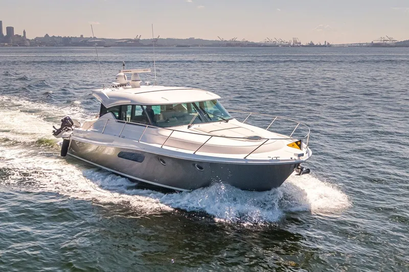 Slide: The Image of 2019 Tiara Yachts C44 Coupe cruising on open water, city skyline in background. - 52