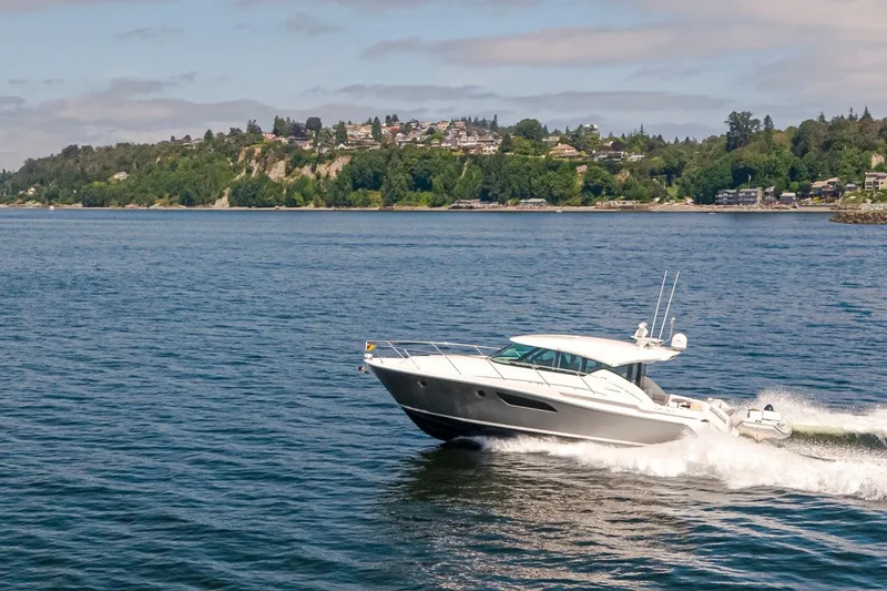 Slide: The Image of 2019 Tiara Yachts C44 Coupe cruising on a scenic lake with lush shoreline. - 44