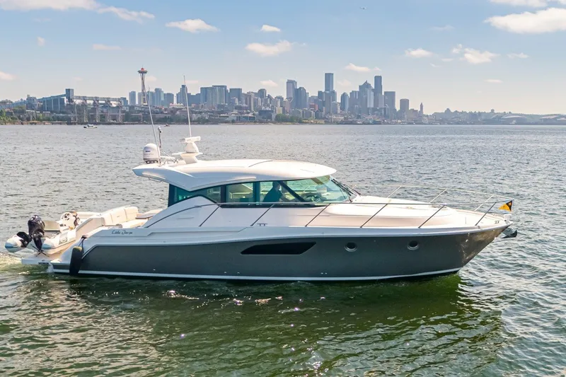 Slide: The Image of 2019 Tiara Yachts C44 Coupe cruising on water with city skyline backdrop. - 1
