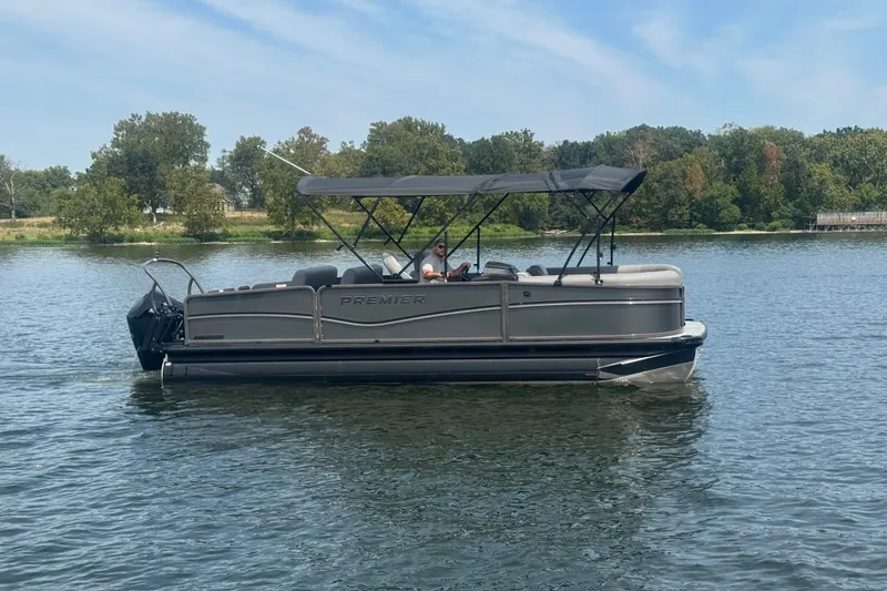 Slide: The Image of 2027 Premier 230 Sunsation RL - CL pontoon boat cruising on a serene lake. - 2
