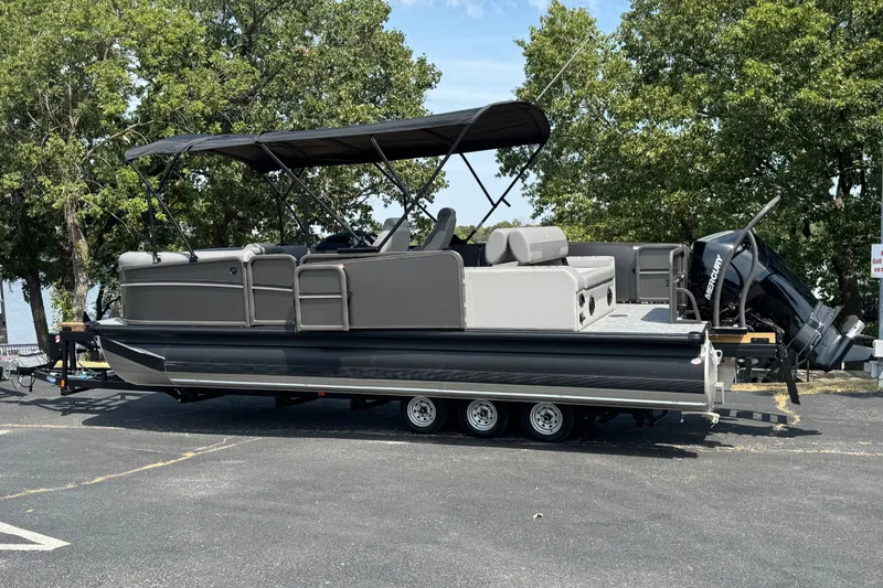 Slide: The Image of 2027 Premier 230 Sunsation RL - CL pontoon boat on trailer, parked near trees. - 3