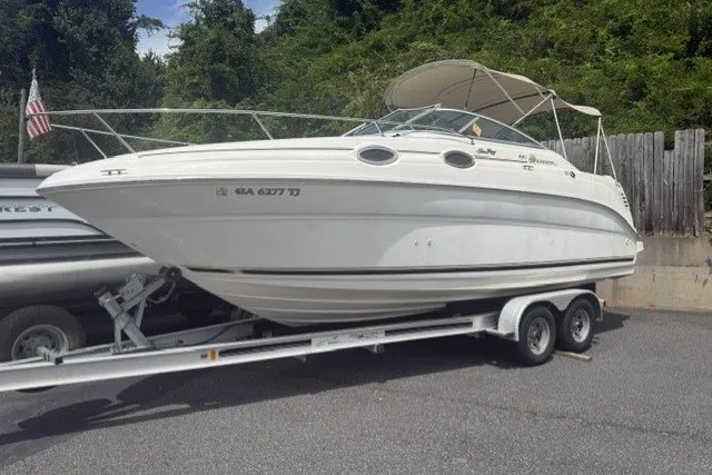 The Image of 2000 Sea Ray 240 Sundancer boat on trailer, parked outdoors with trees in background. - 1