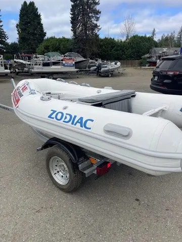 The Image of A white Zodiac inflatable boat on a trailer, surrounded by trees and other boats. - 1