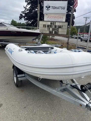 Slide: The Image of A white inflatable boat on a trailer is parked in a lot. Boats and a sign are visible in the background. - 3