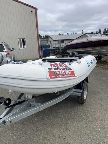 Slide: The Image of A Zodiac Nomad Rib Alu 2.7 boat on a trailer, parked in front of a building. - 11