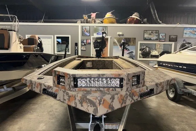 Slide: The Image of 2026 Xpress Bayou 180 boat with camouflage design in showroom setting. - 2