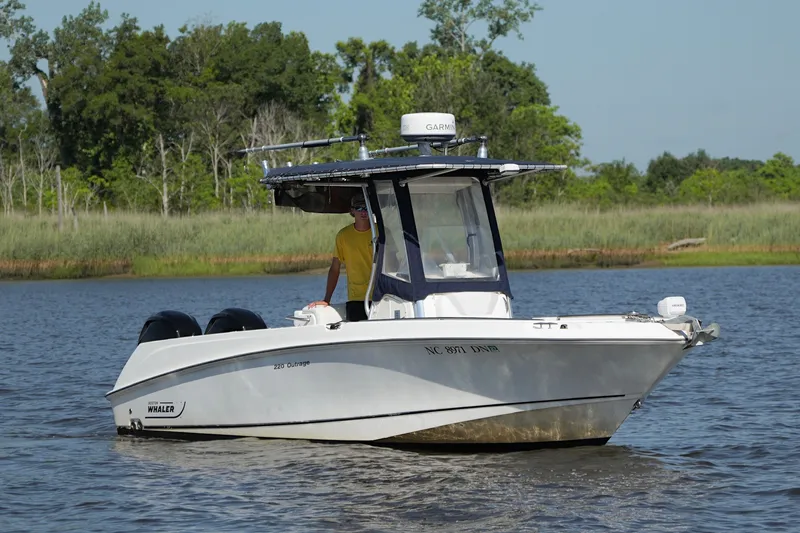 The Image of 2009 Boston Whaler 220 Outrage boat cruising on a calm lake with lush greenery. - 1