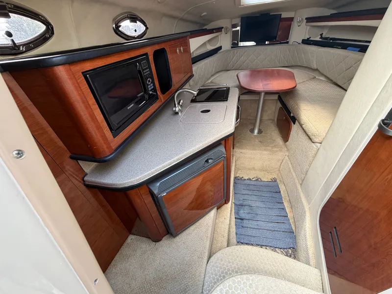 Slide: The Image of The cabin of a 2006 Sea Ray Sundancer 260 features a cozy seating area, a small kitchenette with a microwave and fridge, and a table. - 3