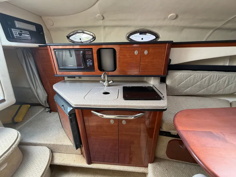 Slide: The Image of The interior of a 2006 Sea Ray Sundancer 260 features a compact kitchen with a microwave, sink, and fridge. - 13