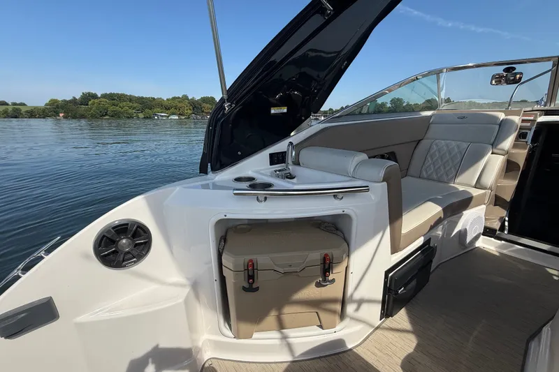 Slide: The Image of 2018 Regal 28 Express boat interior with seating, sink, and storage on a calm lake. - 16