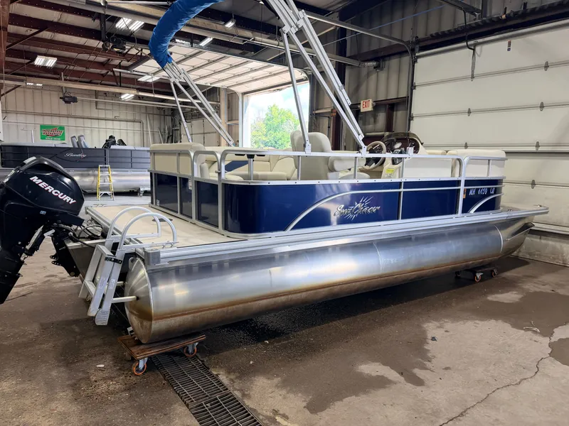 Slide: The Image of A blue SunChaser pontoon boat in a warehouse. It features a canopy and a Mercury engine. - 47