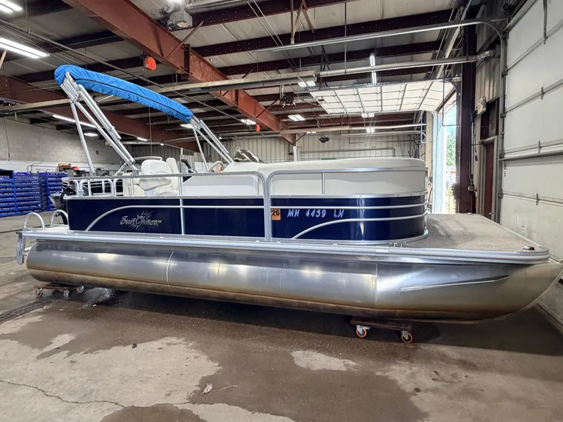Slide: The Image of A 2015 SunChaser pontoon boat with a blue canopy is parked in a warehouse. - 50