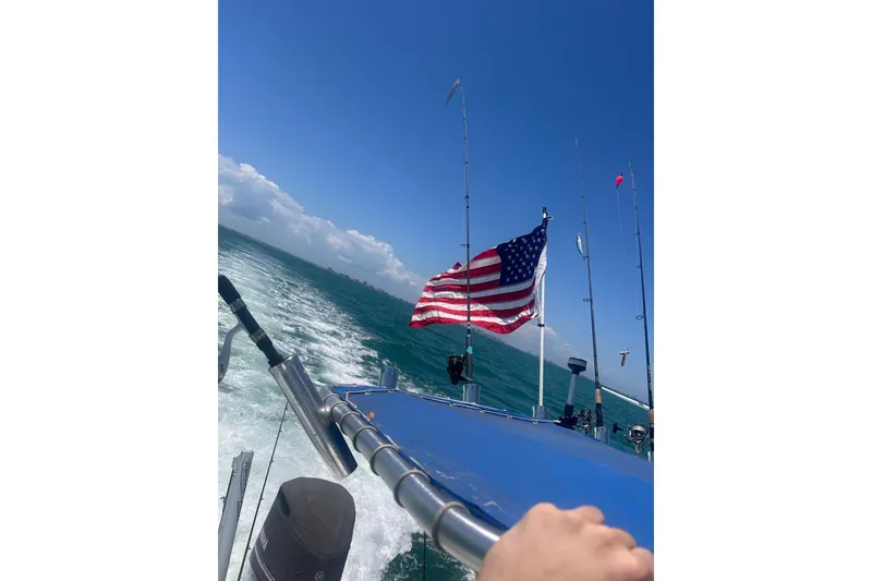Slide: The Image of 2014 Blue Wave 2300 PureBay boat cruising with American flag and fishing rods. - 10