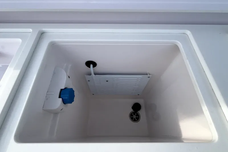 Slide: The Image of Storage compartment in 2023 Axopar 37 XC Cross Cabin boat, featuring a drain and blue valve. - 37